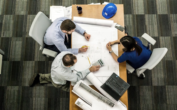 architecture engineering construction professionals working and collaborating on blueprints on desk